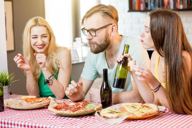 Jeunes amis vêtus avec désinvolture de t-shirts colorés en train de déjeuner avec pizza et bière à la maison