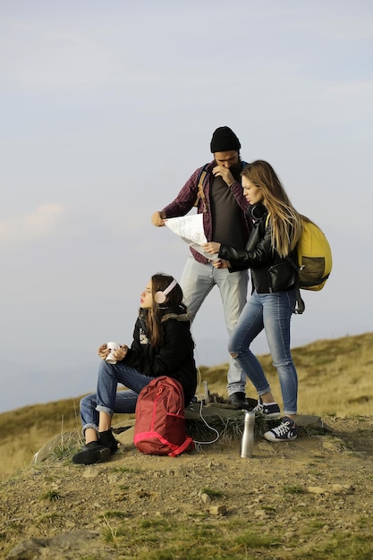 Jeunes amis voyageurs barbu hipster et deux jolies filles femmes avec carte explorent l'itinéraire à l'extérieur au sommet de la montagne sur ciel brumeux