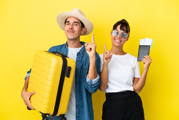 Jeunes amis voyageurs tenant une valise et un passeport isolés sur fond jaune montrant et levant un doigt en signe du meilleur