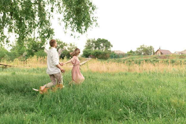 Jeunes amoureux de couple s'amusant et courant sur l'herbe verte sur la pelouse avec leur race de chien domestique bien-aimée Beagle et un bouquet de fleurs sauvages