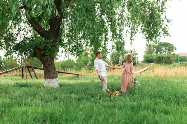 Jeunes amoureux de couple s'amusant et courant sur l'herbe verte sur la pelouse avec leur race de chien domestique bien-aimée Beagle et un bouquet de fleurs sauvages