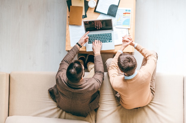 L'un des jeunes analystes en tenue de soirée pointant sur l'écran d'un ordinateur portable tout en présentant de nouvelles données à son collègue