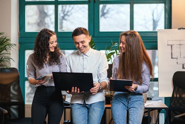 Jeunes architectes ou designers caucasiens utilisant la palette de couleurs pour un nouveau projet sur l'ordinateur portable dans le bureau moderne élégant avec grande fenêtre.