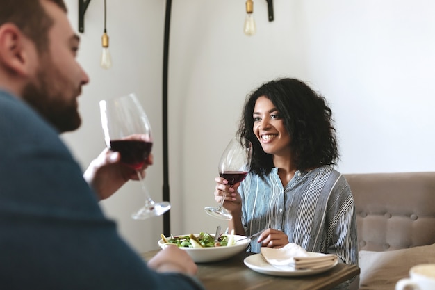 Jeunes assis au restaurant et buvant du vin rouge. Belle fille afro-américaine, manger de la salade et boire du vin au café