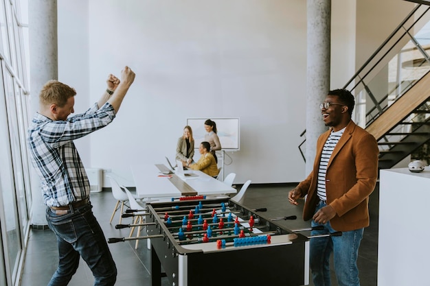 Jeunes beaux hommes d'affaires multiethniques décontractés jouant au baby-foot et se relaxant au bureau