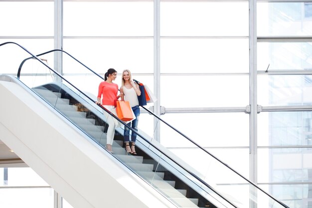 Jeunes belles femmes heureuses sur l'escalator du centre commercial