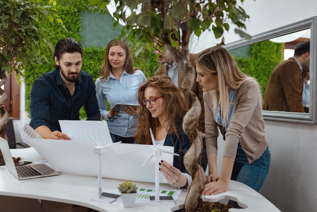 De jeunes collègues d'affaires prospères analysant un projet d'énergie alternative avec des miniatures d'éoliennes à la table, et dans une discussion sérieuse, examinant la paperasse.