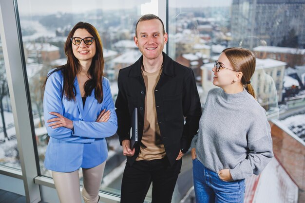 Jeunes collègues étudiants travaillant sur un nouveau projet debout près des fenêtres dans un espace de travail moderne près de la fenêtre Les hommes d'affaires travaillent à distance