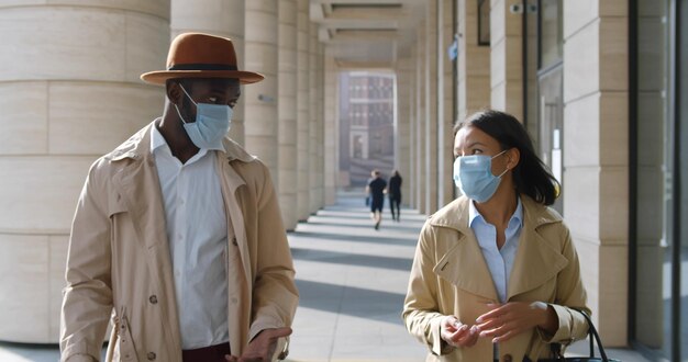 Photo jeunes collègues en masque médical marchant à l'extérieur d'un bâtiment moderne