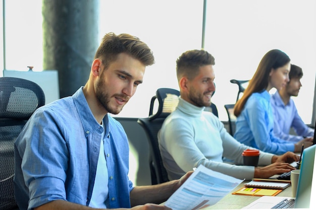 Jeunes collègues modernes en vêtements décontractés intelligents travaillant ensemble tout en passant du temps dans le bureau de création