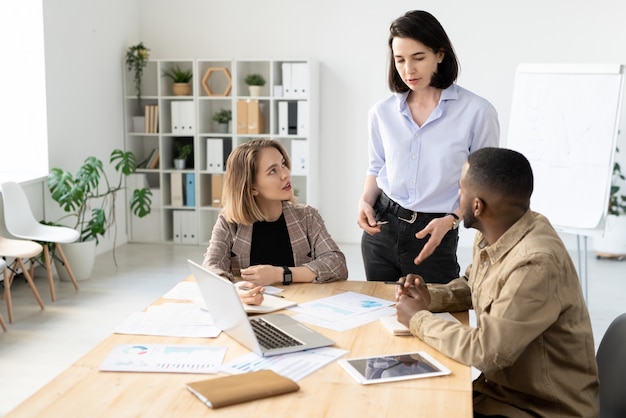 Jeunes collègues multiethniques discutant des données analytiques tout en travaillant sur une nouvelle campagne publicitaire