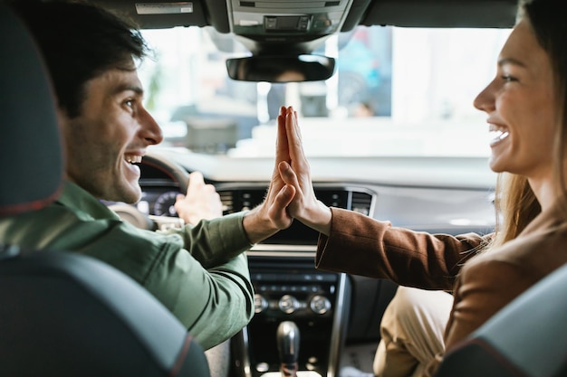 Jeunes conjoints enthousiastes célébrant l'achat d'une nouvelle voiture assis à l'intérieur d'une auto moderne