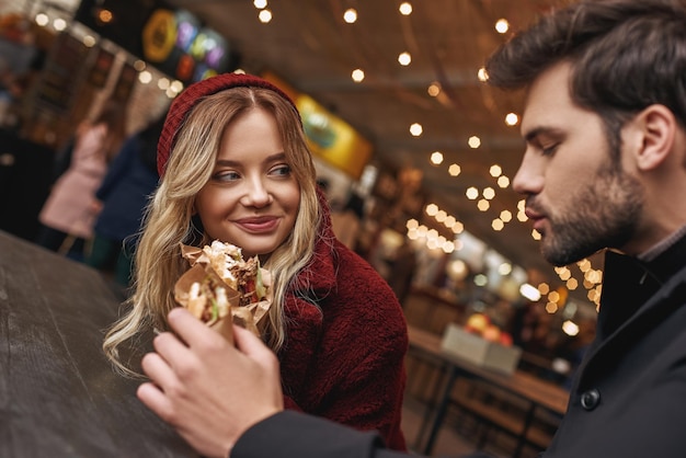 Les jeunes couples mangent dehors tenant des sandwichs au marché de nourriture de rue