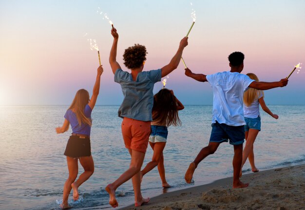 Les jeunes courent sur la plage avec des bougies scintillantes dans les mains