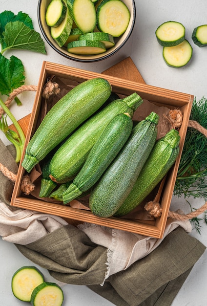 Jeunes courgettes dans une boîte en bois sur fond gris. Vue de dessus, verticale.