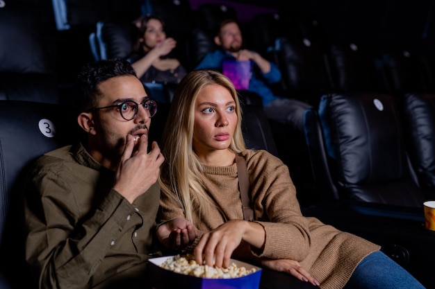 Jeunes dates effrayées avec boîte de pop-corn assis dans un cinéma sombre et regarder un film d'horreur à loisir