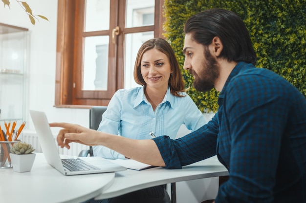 De jeunes designers à succès parlent de projet au bureau. Un homme parle d'un projet exposé sur un ordinateur portable, et une jeune femme écoute son collègue.