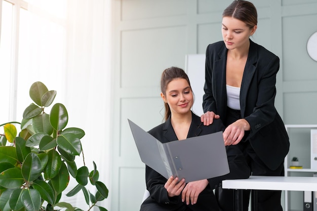 Les jeunes dirigeantes vérifient les états financiers à partir de documents papier. Deux femmes d'affaires confiantes vêtues d'un costume noir au bureau vérifiant un document financier à la recherche d'un dossier et discutant