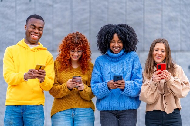 Photo des jeunes divers souriants utilisant le téléphone debout à l'extérieur