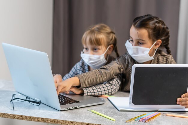 Jeunes écolières avec masque de protection faciale regardant un cours d'éducation en ligne. Concept d'éducation au verrouillage du coronavirus ou du Covid-19.