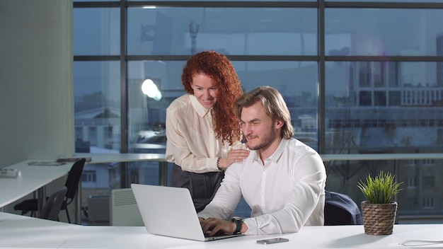 Jeunes employés de bureau discutant d'un projet en ligne à l'aide d'un ordinateur portable au bureau moderne