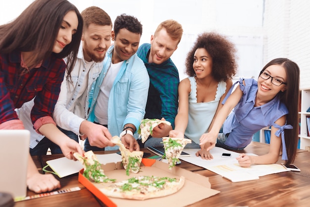 Les jeunes employés mangent une pizza ensemble.