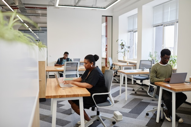 Photo jeunes entrepreneurs noirs travaillant sur des ordinateurs portables à des bureaux dans un centre de coworking en espace ouvert