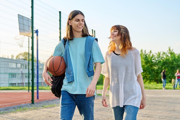 Jeunes étudiantes adolescentes avec ballon marchant en plein air près d'un terrain de basket