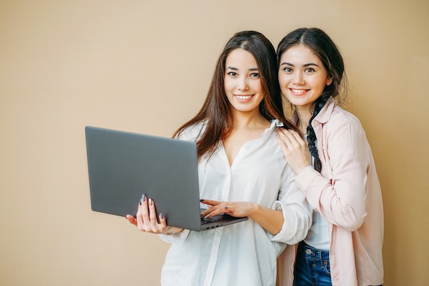 Jeunes étudiants filles souriantes en casual avec ordinateur portable en mains isolé sur fond beige