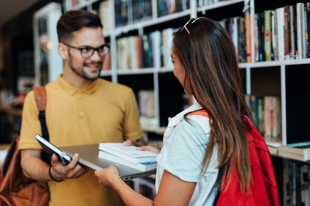 Jeunes étudiants séduisants homme et femme choisissant des livres dans la librairie.