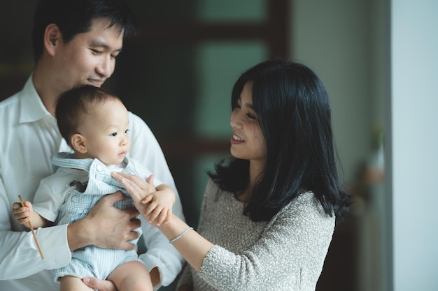 Les jeunes familles asiatiques sont heureuses ensemble à la maison par le concept d'assurance-vie enfant bébé et mère et père s'amusant et souriant avec amour enfance vivant dans un style de vie confortable avec papa et maman
