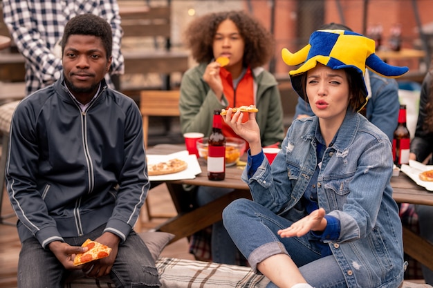 Jeunes fans de football interculturel regardant la diffusion dans un café en plein air pendant que l'un d'eux commente le match