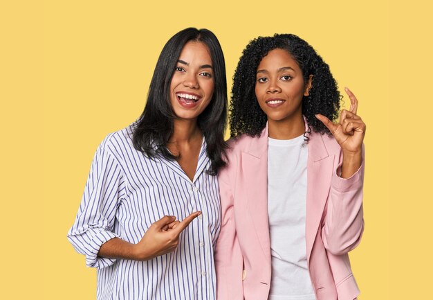 Jeunes femmes d'affaires latines en studio tenant quelque chose de petit avec les index souriants et confiants