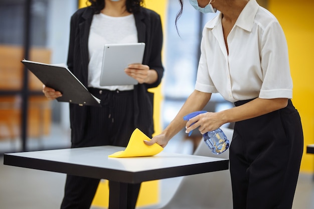 Les jeunes femmes d'affaires nettoient le lieu de travail, essuyez le bureau avec un chiffon jaune.