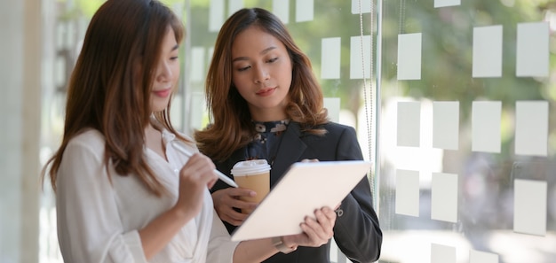 Jeunes femmes d'affaires travaillant sur son projet tout en utilisant une tablette numérique