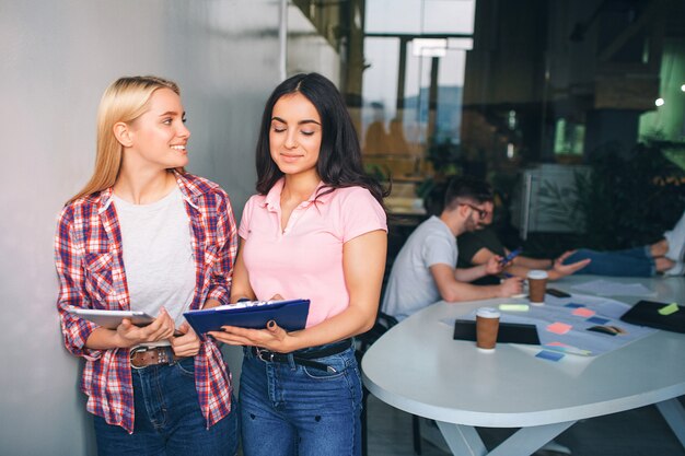 Les jeunes femmes agréables et positives se tiennent ensemble dans la salle blanche