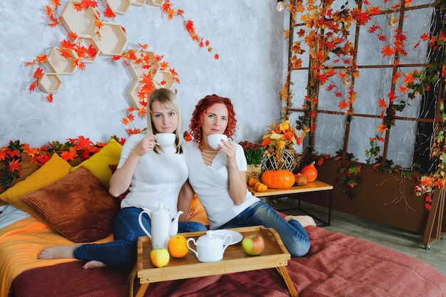 jeunes femmes, amis, soeurs assis dans un lit douillet. tasses à thé, boire du thé en chandail. Automne