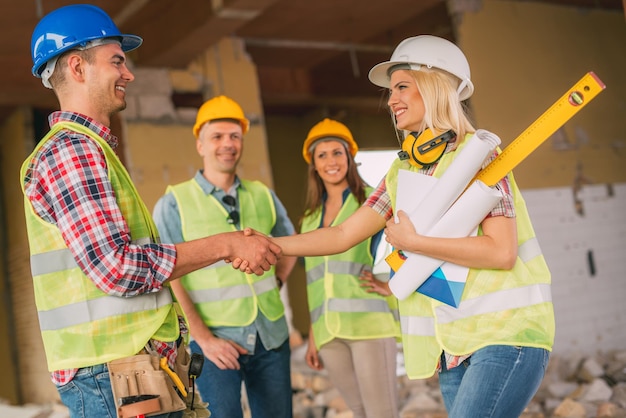 Jeunes femmes architectes de construction et électriciennes se serrant la main dans le bâtiment endommagé par la catastrophe alors qu'en arrière-plan se tenaient leurs collègues.