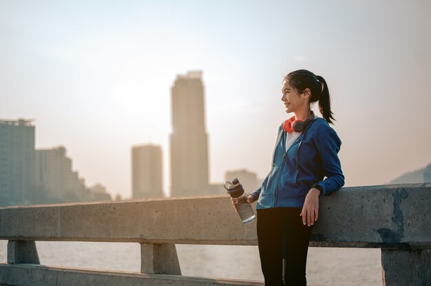 Les jeunes femmes asiatiques boivent de l'eau et se reposent après avoir fait du jogging une séance d'entraînement matinale dans la ville