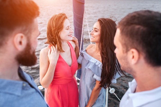 Photo des jeunes femmes attirantes et incroyables se tiennent ensemble et se regardent. ils sourient. les hommes se tiennent devant eux et regardent les femmes.