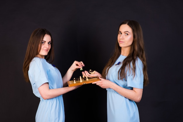 Les jeunes femmes aux cheveux noirs dans une robe bleue jouent aux échecs sur un mur jaune et noir