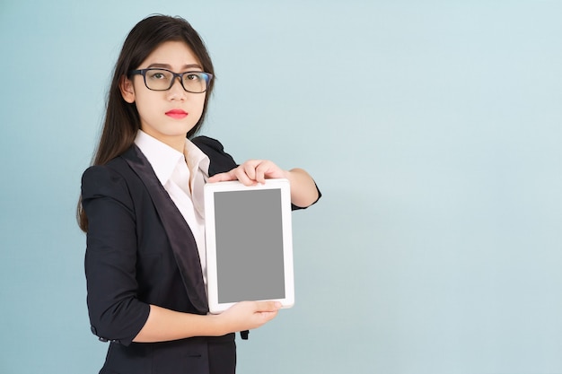 Jeunes femmes en costume tenant sa tablette numérique debout sur fond bleu