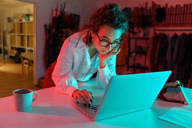 Les jeunes femmes créatrices de vêtements travaillent sur un ordinateur portable dans un atelier studio lisent les e-mails commerciaux et passent des commandes