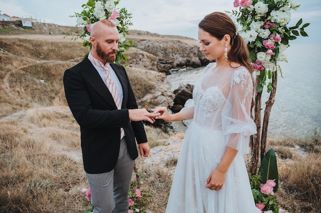 Les jeunes femmes dans une robe blanche met une bague au doigt d'un homme dans une cérémonie de mariage de costume