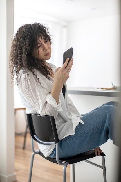 Les jeunes femmes domestiques dactylographient un message texte communiquent les réseaux sociaux à la cuisine nordique blanche