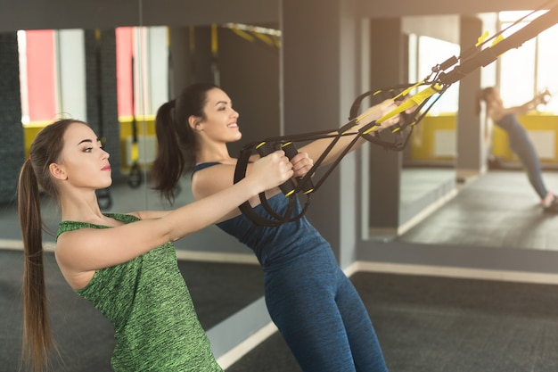 Jeunes femmes effectuant une formation de suspension dans une salle de sport. Filles sportives faisant des exercices d'étirement avec une corde élastique, espace de copie