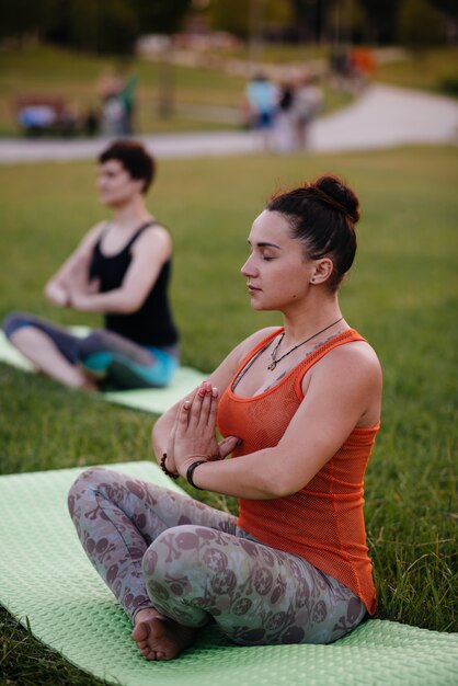 Les jeunes femmes font du yoga en plein air dans le parc pendant le coucher du soleil. Mode de vie sain