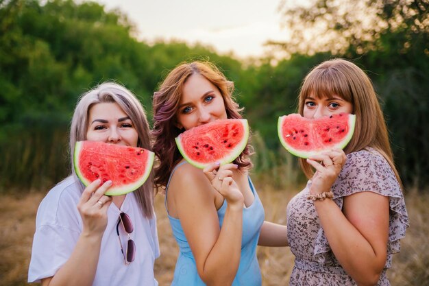 De jeunes femmes heureuses tiennent des tranches de pastèque à l'extérieur Des baies rouges vives Une collation sucrée juteuse en été lors d'un pique-nique