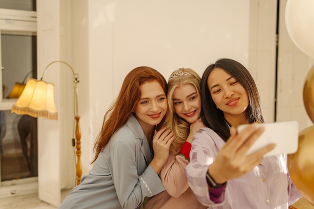 Jeunes femmes interraciales positives souriant tendrement tout en prenant un selfie lors d'une soirée pyjama Concept de féminité et de beauté