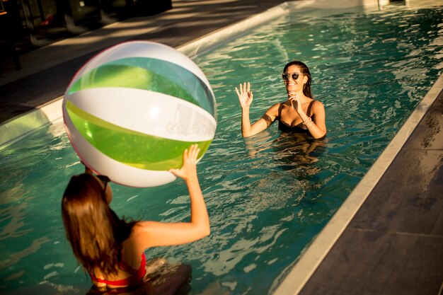 Jeunes femmes jouant avec un ballon dans la piscine à la journée ensoleillée
